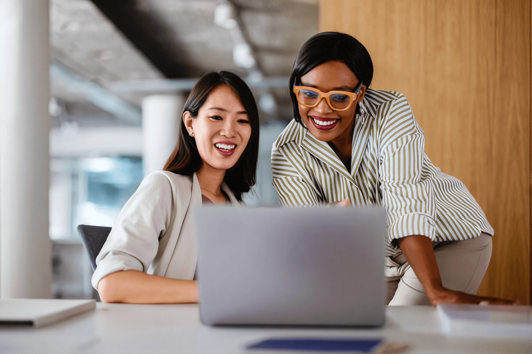 Two smiling colleagues working together at a laptop in a modern office setting