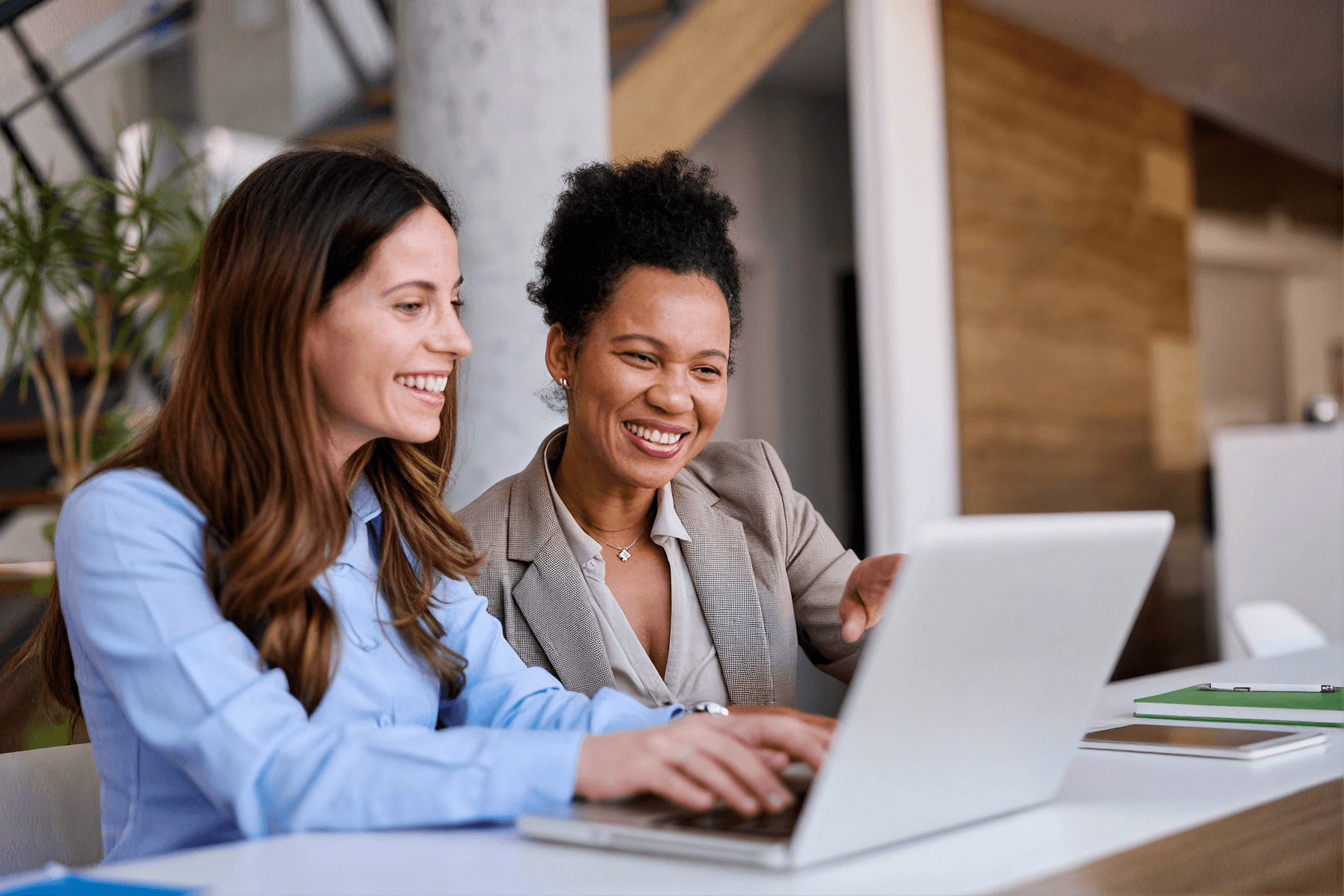 Two colleagues smiling while working together at a laptop in a modern office space